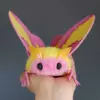 Close-up of Rosy Maple Moth plush doll face with big black eyes and fluffy pink head