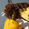 Close-up of yellow Garden Tiger Moth head: brown-and-yellow faux fur, beaded eyes, white feather antennae, wire legs — on yellow pumpkin.