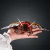 Front view of handmade Garden Tiger Moth doll in open hand: brown faux fur body, red collar, beaded eyes, yellow wings with blue spots and brown/white camo wings.