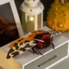 Red-collared Garden Tiger Moth doll on a grey drawer, with yellow wings (blue spots) and brown/white camo wings, faux fur body, beaded eyes.
