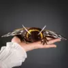 Front view of yellow Garden Tiger Moth doll in open hand: brown-and-yellow faux fur body with yellow stripe, beaded eyes, white feather antennae, polymer clay wings.