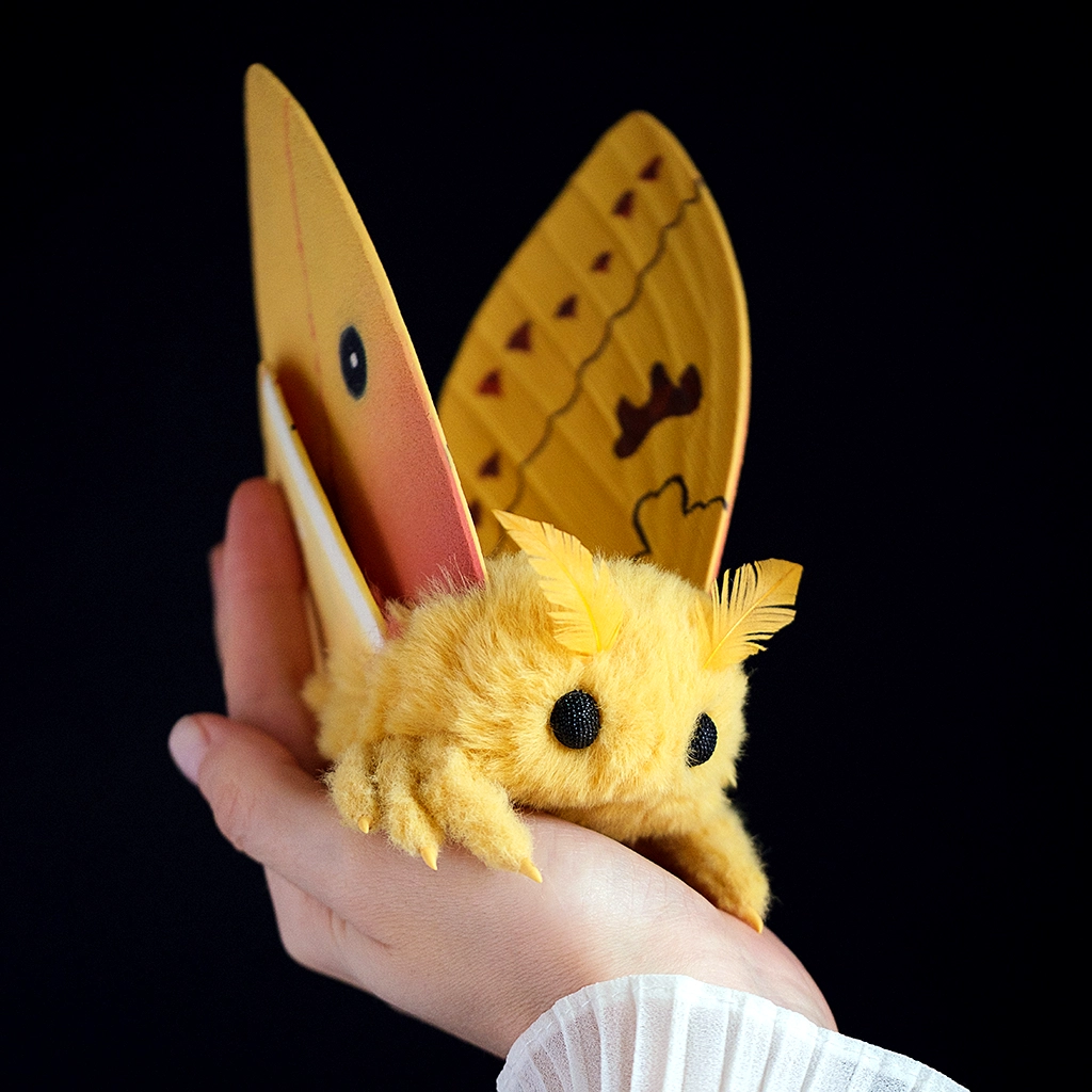 Handmade Io Moth art doll with golden-yellow wings held in a hand